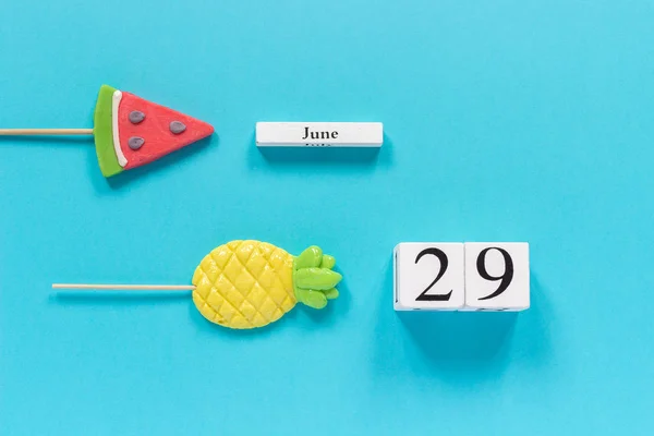 Деревянные кубики календарь даты 29 июня и летом фрукты конфеты ананас, арбуз леденцы на палочке на синем фоне. Концепция отдыха или праздники Creative Top view Flat lay Template — стоковое фото