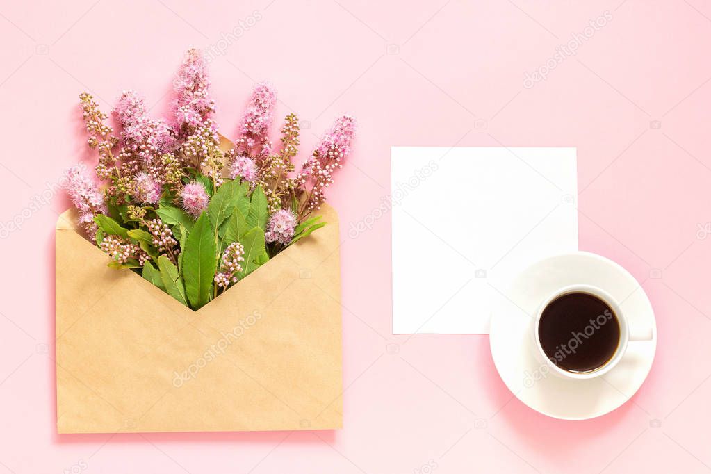 Bouquet of pink flowers in envelope, cup of coffee and a white blank card for text on pink background Concept Good morning or Women's day