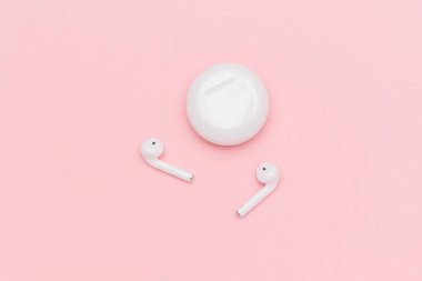 Beyaz kablosuz Bluetooth kulaklıklar ve pembe kağıt arka plan üzerinde şarj kılıfı. Metin veya tasarım için şablon. Düz lay Üstten görünüm Kopyalama alanı
