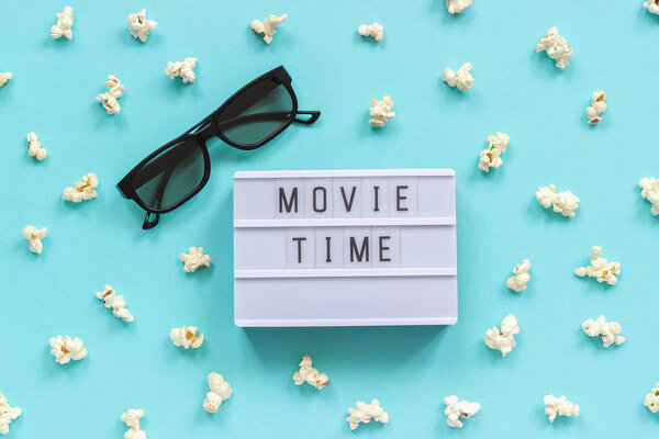 3D glasses, popcorn and lightbox text Movie time on blue paper background. Top view Template Concept cinema movie and entertainment