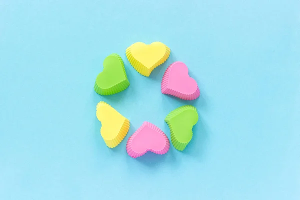 Moldes coloridos em forma de coração de silicone prato para assar cupcakes no fundo de papel azul. Modelo para lettering, texto ou seu design Vista superior, espaço de cópia — Fotografia de Stock