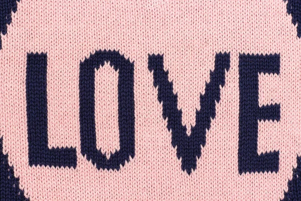 Χειροποίητο ροζ πλεκτό ύφασμα με μπλε λέξη Love δεσμεύεται σε βελόνες πλεξίματος ως πίσω ή υφή. Κορυφαία προβολή — Φωτογραφία Αρχείου