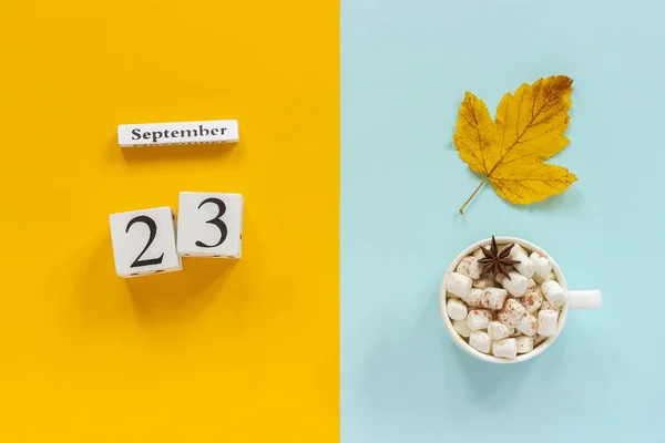 Осенняя композиция. Деревянный календарь 23 сентября, чашка какао с зефиром и желтыми осенними листьями на желтом синем фоне. Вид сверху Концепция макета квартиры — стоковое фото