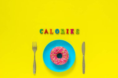 Kalori ve Pembe donut mavi plaka ve sarı arka plan üzerinde bıçak çatal.