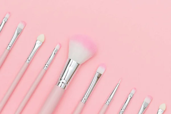 Set of pink makeup brushes on pastel pink background. Top-down composition, copy space