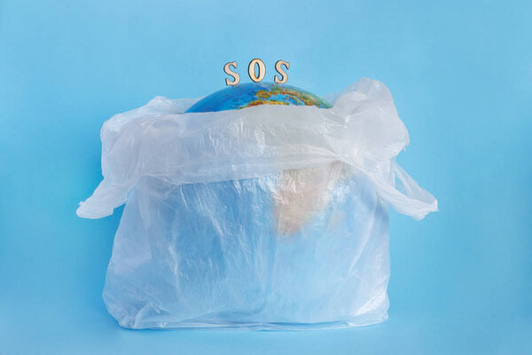 planet Earth in plastic bag and inscription SOS, blue background