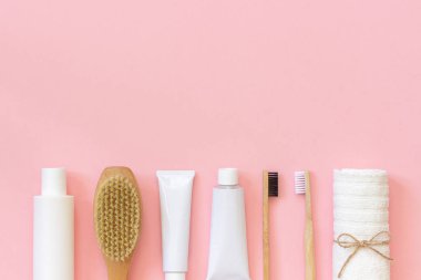 Duş veya banyo bambu diş fırçası, doğal fırça, beyaz şişeler, vücut için havlu aksesuarları, pembe arka planda yüz ve diş bakımı için eko kozmetik ürünleri ve araçları seti. Kopya alanı, Üstgörünüm