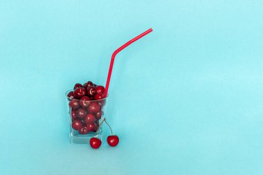 Mavi arka plan üzerinde saman ile cam kırmızı olgun tatlı kiraz. Kavram taze doğal meyve suyu, smoothies, sağlıklı beslenme veya diyet