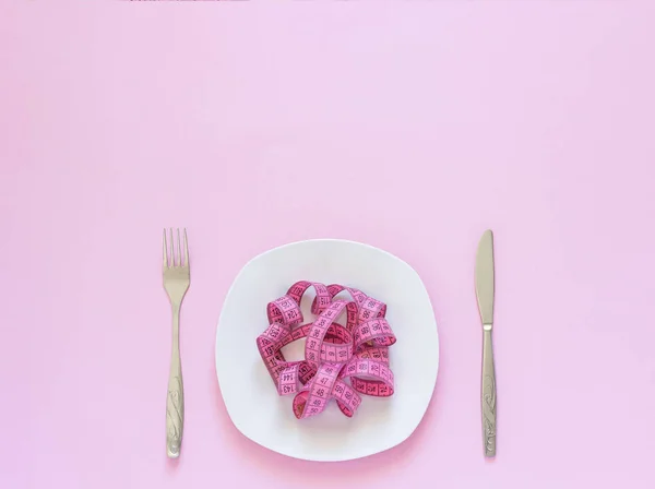 Cinta métrica rosa acostada en placa en forma de espagueti, cuchillo y tenedor sobre fondo rosa — Foto de Stock