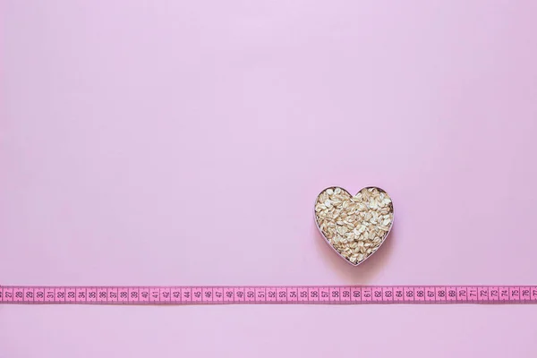 Ovesné vločky ve tvaru srdce na měřicí pásce na růžovém pozadí. — Stock fotografie
