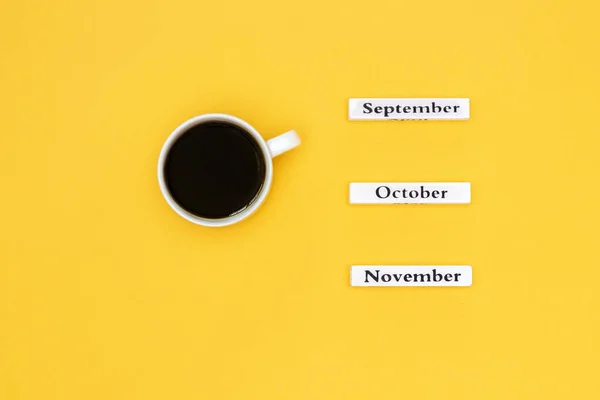 Cup of coffee and calendar November October September on yellow background — Stock Photo, Image