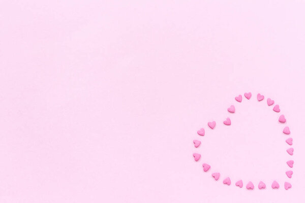 Pink confectionery sprinkles in heart shape on pastel pink background. Concept Valentine's card. Top view Copy space for text