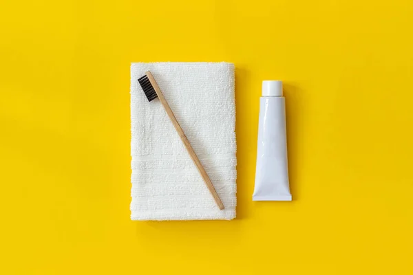 Natürliche umweltfreundliche Bambusbürste auf weißem Handtuch und einer Tube Zahnpasta. Set zum Waschen auf Papier gelbem Hintergrund. Kopierraum für Text oder Ihre Designoberseite flach legen — Stockfoto