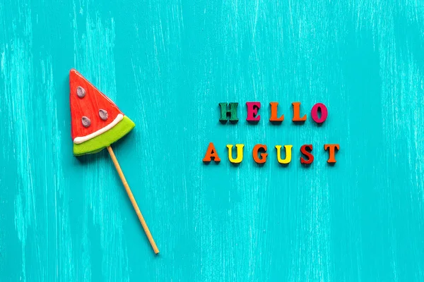 Hallo August Text aus bunten Buchstaben und Wassermelonen-Lutscher auf Stick auf blauem Holzgrund. Konzept kreative Draufsicht Vorlage Grußkarte — Stockfoto