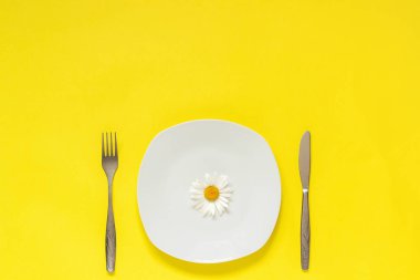 Plaka üzerinde bir çiçek papatya papatya, sarı kağıt arka plan üzerinde çatal çatal çatal bıçak Kavram vejetaryen sağlıklı beslenme diyet veya anoreksiya Yaratıcı üst görünüm Metin veya tasarım için alan şablonu kopyalayın