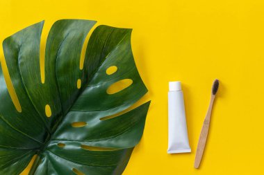 Doğal çevre dostu bambu fırça, diş macunu ve tropikal eaf monstera tüp. Kağıt sarı arka plan üzerinde yıkama için ayarlayın. Üstten düz yatıyordu