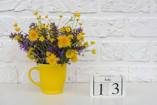 Calendario de cubos de madera 13 de julio y copa amarilla con flores de colores brillantes contra la pared de ladrillo blanco. Plantilla calendario fecha para su diseño Copiar espacio —  Fotos de Stock