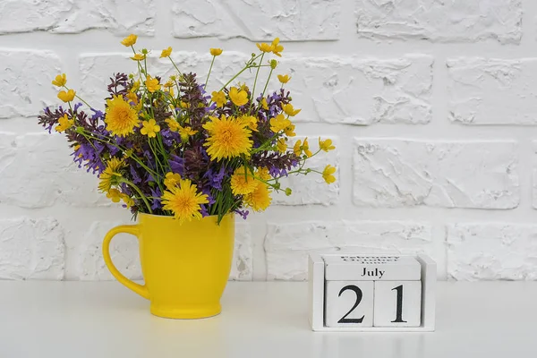 Calendario de cubos de madera 21 de julio y copa amarilla con flores de colores brillantes contra la pared de ladrillo blanco. Plantilla calendario fecha para su diseño Copiar espacio —  Fotos de Stock