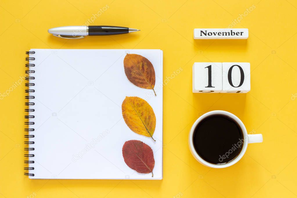 calendar November 10 cup of coffee, notepad with pen and yellow leaf on yellow background