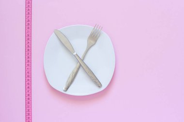 Pembe arka planda beyaz plaka ve bant ölçümü üzerinde çapraz çatal ve bıçak.