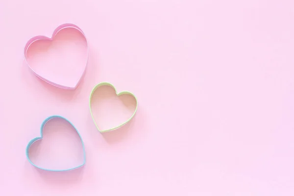 Cortadores de colores galletas en forma de corazón sobre fondo rosa pastel. Concepto tarjeta de San Valentín. Vista superior Copiar espacio para texto —  Fotos de Stock