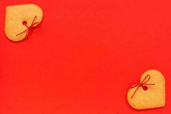 Galletas de jengibre en forma de corazón decoradas con un lazo sobre un fondo rojo. Vista superior Copiar espacio Tarjeta San Valentín — Foto de Stock