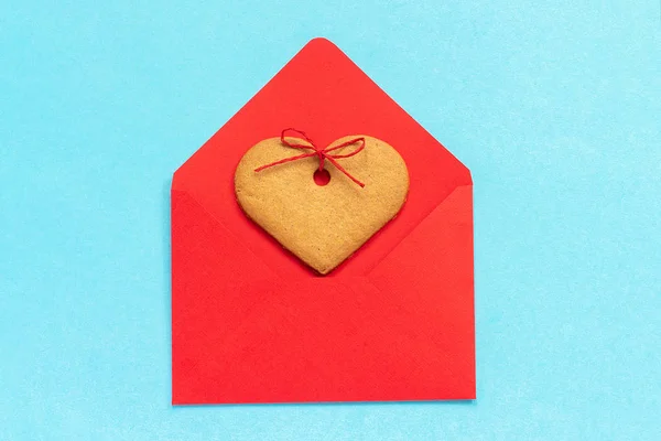 Червоний конверт і імбирне печиво у формі серця на синьому фоні . — стокове фото