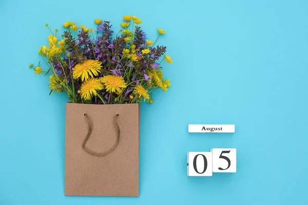 Wooden cubes calendar August 5 and field colorful rustic flowers in craft package on blue background. Greeting card Flat Lay Concept Hello August Template with copy space for text and design — Stock Photo, Image