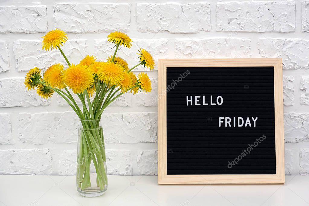 Hello Friday words on black letter board and bouquet of yellow dandelions flowers on table against white brick wall. Concept Happy Monday. Template for postcard