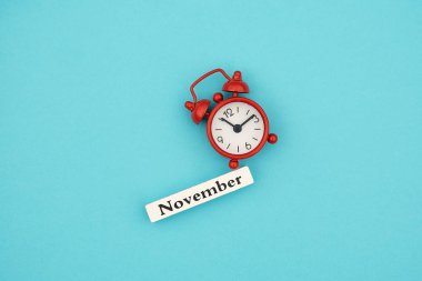 Ahşap takvim sonbahar ay Kasım ve mavi kağıt arka plan üzerinde kırmızı çalar saat. Konsept Merhaba Eylül. Yaratıcı Üst görünüm Flat Lay Minimal tarzı
