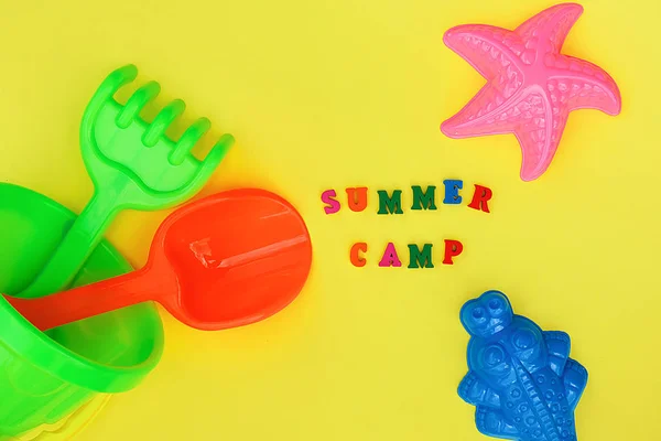 Text Summer camp and multicolored set children's toys for summer games in sandbox or on sandy beach on yellow background. Creative top view Flat lay Concept children's rest and development