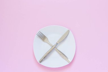 Pembe arka plan üzerinde beyaz plaka üzerinde çapraz çatal ve bıçak.