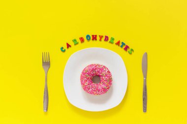 Metin karbonhidratlar, tabakta pembe donut ve çatal masa bıçağı çatalı. Kavram sağlıksız diyet