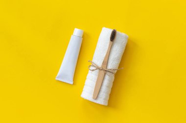 Beyaz havlu ve diş macunu tüp doğal çevre dostu bambu fırça. Kağıt sarı arka plan üzerinde yıkama için ayarlayın. Metin veya tasarım Üst görünüm Düz lay için kopya alanı