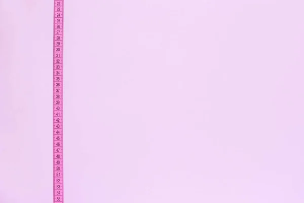 Pink tape measure vertically crosses pink background. — Stock Photo, Image