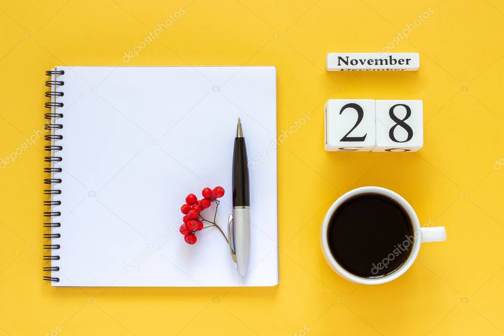 calendar November 28 cup of coffee, notepad with pen and yellow leaf on yellow background