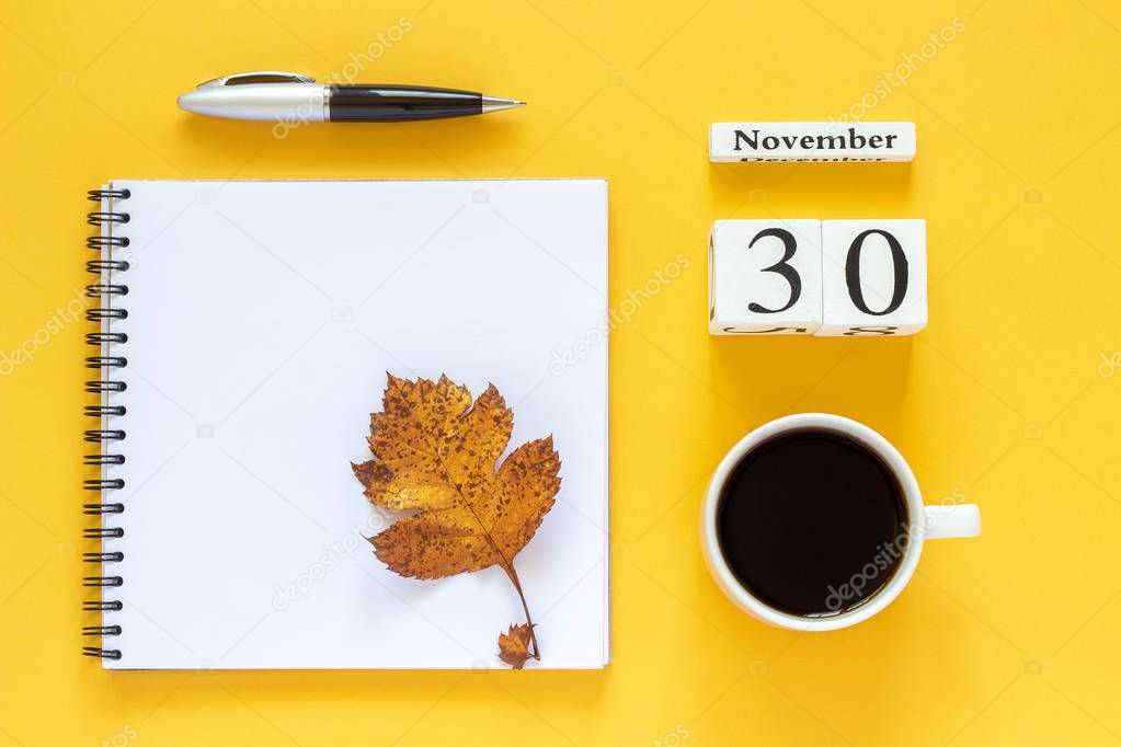 calendar November 30 cup of coffee, notepad with pen and yellow leaf on yellow background