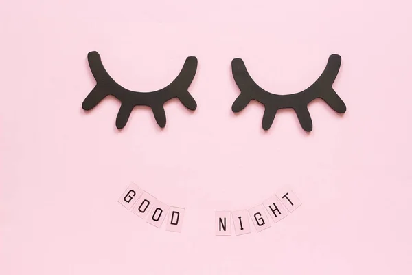 Text Good Night and decorative wooden black eyelashes, closed eyes on pink paper background. Concept Sweet dreams Greeting card Top view Creative flat lay — Stock Photo, Image