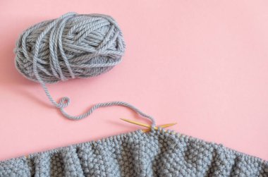 İplik topu ile iğneler üzerinde gri örme kumaş parçası, pembe arka plan üzerinde örgü işlemi. Metin için alan kopyalama. Üst görünüm Düz döşeme Şablonu tasarımınız için