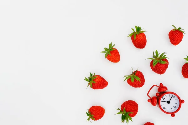 Reloj despertador rojo y fresas que vuelan esparciendo bayas sobre fondo blanco. Vista superior, plano, espacio de copia. Concepto dieta y tiempo de desintoxicación o tiempo de menú de verano. Plantilla para texto, diseño, invitación —  Fotos de Stock