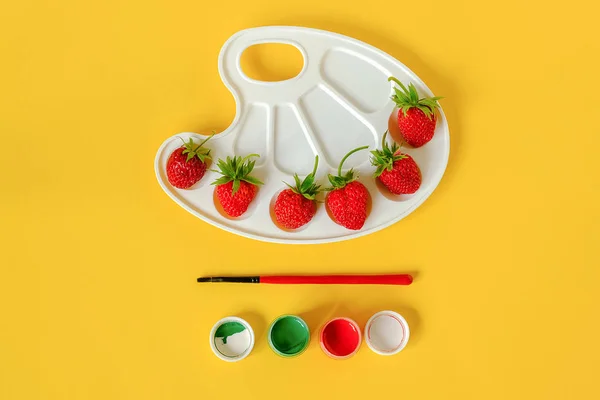 Fresas rojas maduras en una paleta artística, pincel y gouache sobre fondo amarillo con espacio para copiar. Concepto creativo pintura de colores de verano. Plantilla de laico plano para invitación de postales de diseño — Foto de Stock