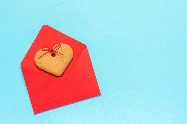 Enveloppe rouge et biscuits au gingembre en forme de coeur sur fond bleu . — Photo