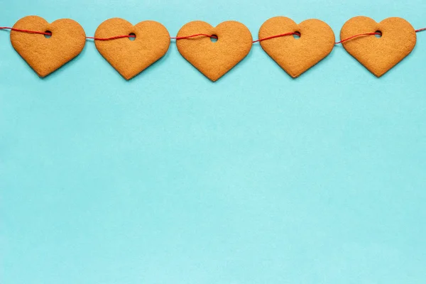 Guirnalda de galletas de jengibre en forma de corazones en cinta roja, situada en la parte superior del borde del marco sobre fondo azul. Vista superior Copiar espacio Tarjeta San Valentín —  Fotos de Stock