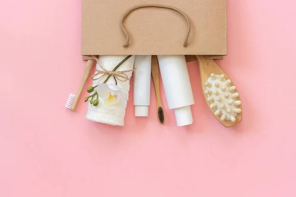 Set of eco cosmetics products and tools for shower or bath Bamboo toothbrush, natural brush, white bottles, towel accessories for body, face and teeth care in paper bag on pink background. Copy space