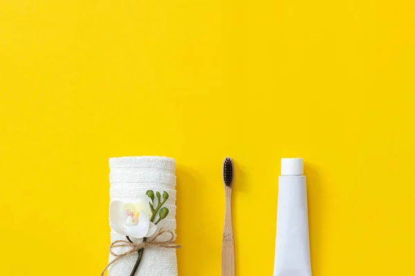 Natürliche umweltfreundliche Bambusbürste, weißes Handtuch und eine Tube Zahnpasta. Set zum Waschen auf Papier gelbem Hintergrund. Kopierraum für Text oder Ihre Designoberseite flach legen — Stockfoto