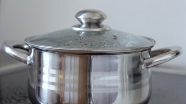 Cam kapaklı bir tencerede kaynar su. Su gurgles, serpin ve tavadan akar
