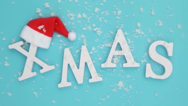 Text Weihnachten aus Band weißen Buchstaben in roter Weihnachtsmütze und fallendem Schnee auf blauem Hintergrund. Konzept frohe Weihnachten. von oben flach liegend — Stockvideo