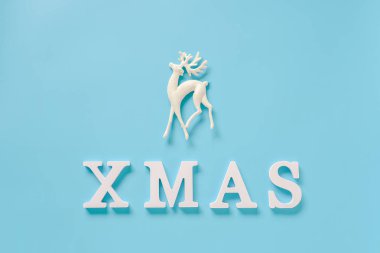 Mavi arka planda beyaz harfler ve Noel dekorasyon geyik oyuncak gelen metin Xmas. Konsept mutlu Noeller. Minimal stil üst görünüm düz tasarım, kart, davetiye için şablon yatıyordu