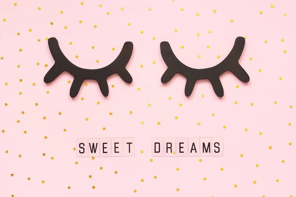 Text Sweet dreams and decorative wooden black eyelashes, closed eyes gold star on pink paper background. Concept Good night Greeting card Top view Creative flat lay