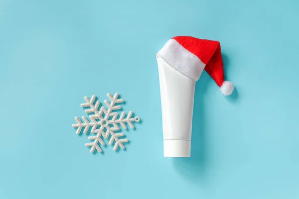 Cosmético, tubo médico branco para creme, pomada ou outro produto em chapéu vermelho Papai Noel e floco de neve branco no fundo azul. Conceito pele de inverno e cuidados com o corpo ou presente de xmas. Modelo Mockup — Fotografia de Stock